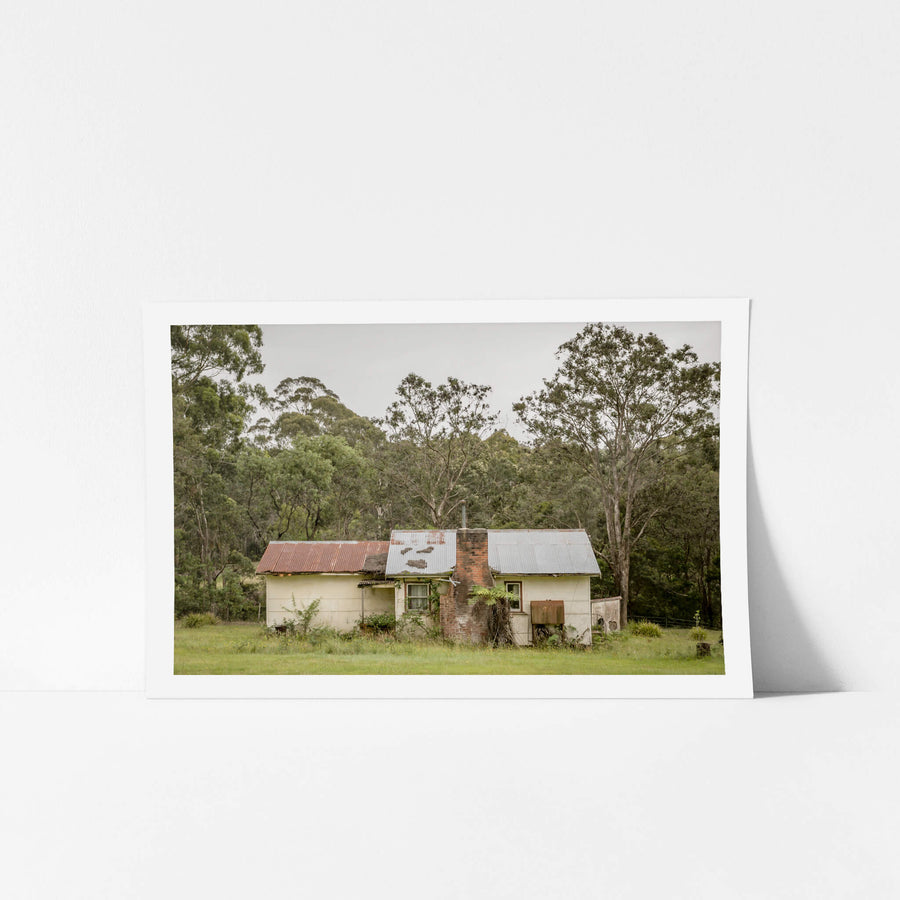 Lochview Cottage at A Place to Call Home, a small weatherboard cottage sits low in a flat green clearing, backed by dense.
