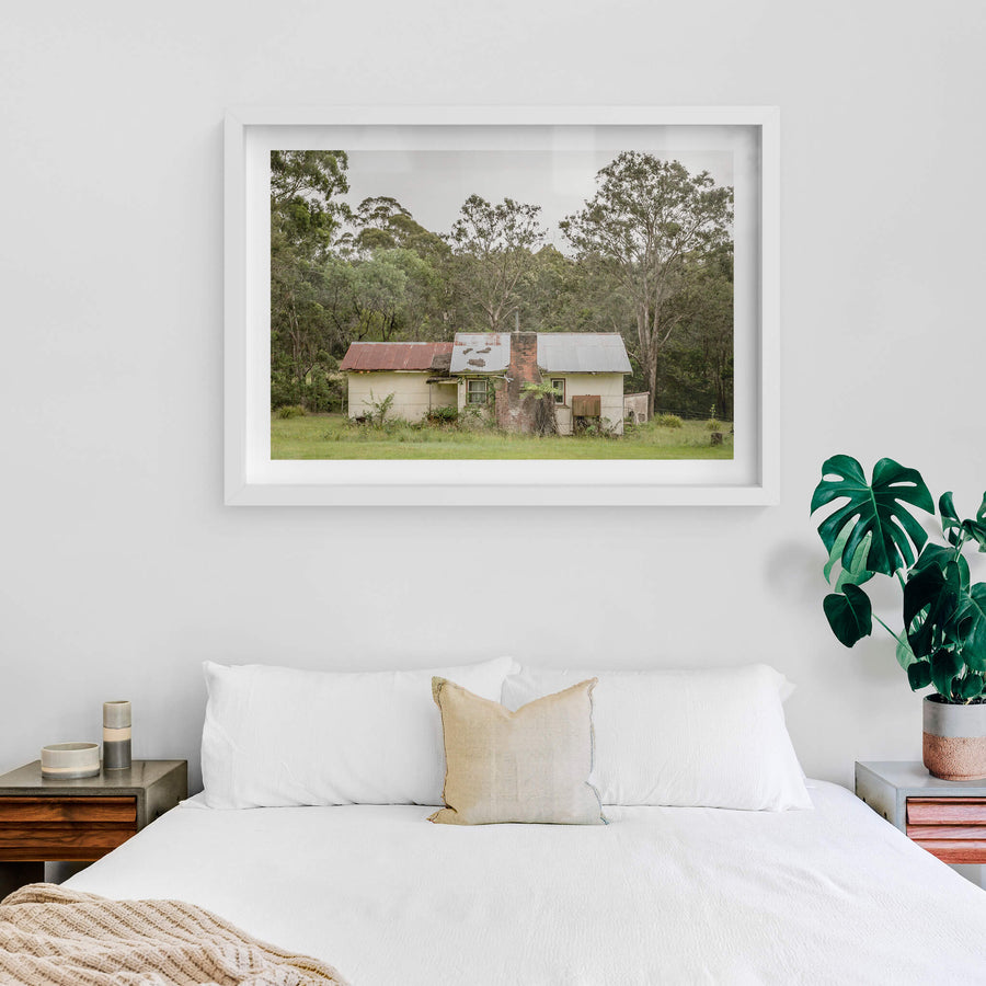 Lochview Cottage at A Place to Call Home, a small weatherboard cottage sits low in a flat green clearing, backed by dense.