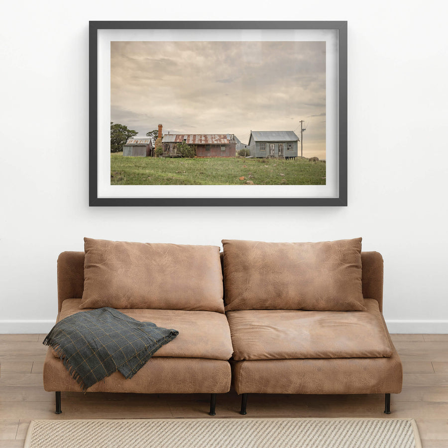 Numbla Vale Buildings at A Place to Call Home, a cluster of buildings sits on a green rise under heavy, layered cloud.