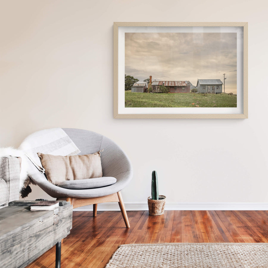 Numbla Vale Buildings at A Place to Call Home, a cluster of buildings sits on a green rise under heavy, layered cloud.