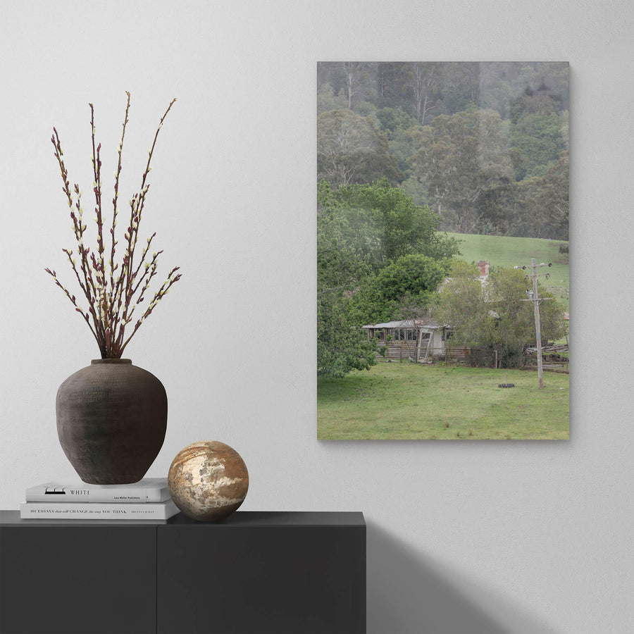 Reclaimed Home at A Place to Call Home, a weatherboard farmhouse sits low in a valley of green pasture, half-swallowed.