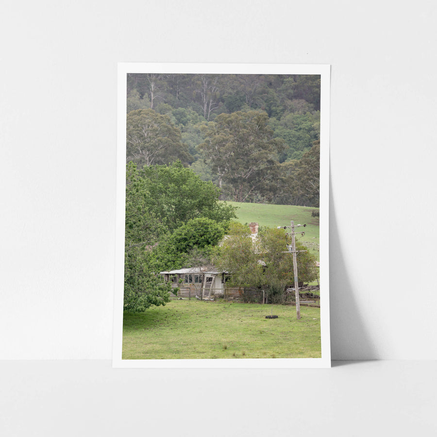 Reclaimed Home at A Place to Call Home, a weatherboard farmhouse sits low in a valley of green pasture, half-swallowed.