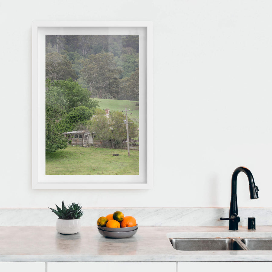 Reclaimed Home at A Place to Call Home, a weatherboard farmhouse sits low in a valley of green pasture, half-swallowed.