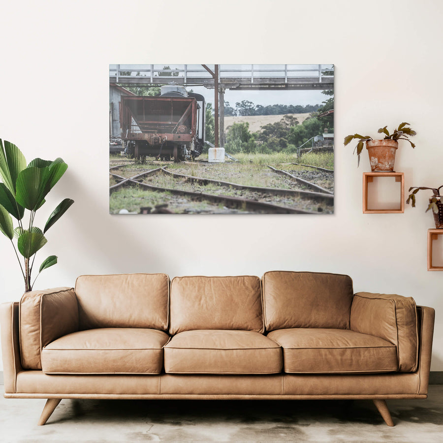 Upline at Bombala Station, a rusted hopper wagon sits low on the sidings beneath a steel and timber footbridge.