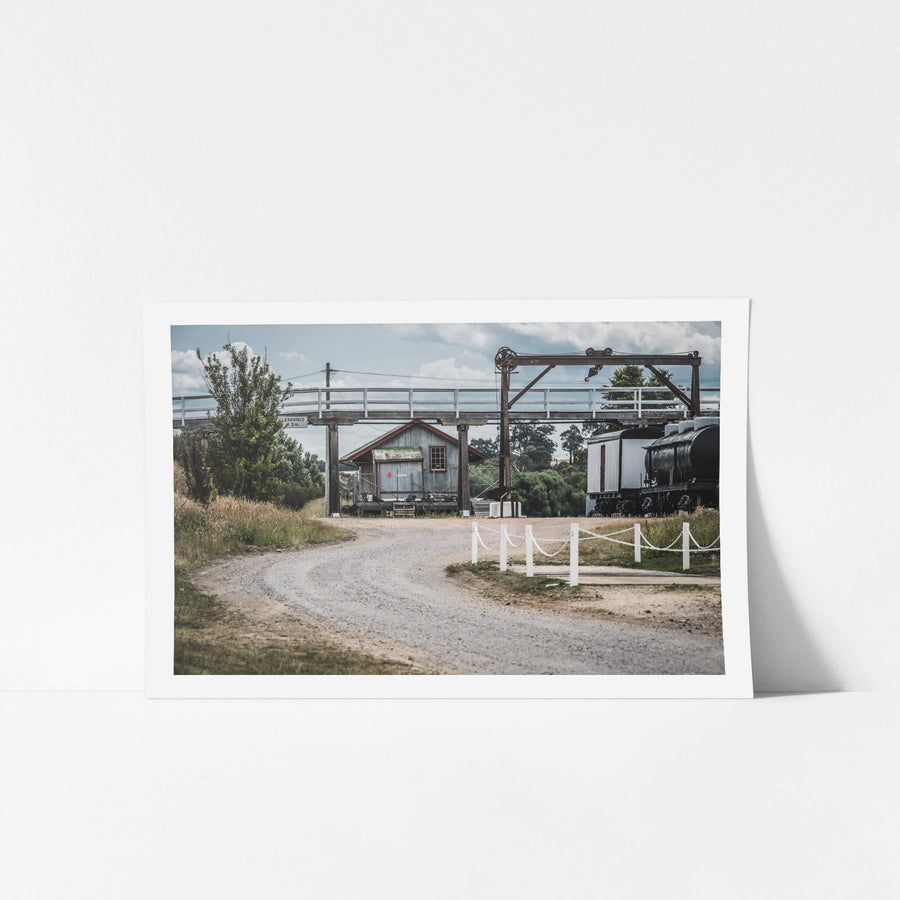 Yard at Bombala Station, a gravel road curves beneath a steel overhead crane and timber footbridge.