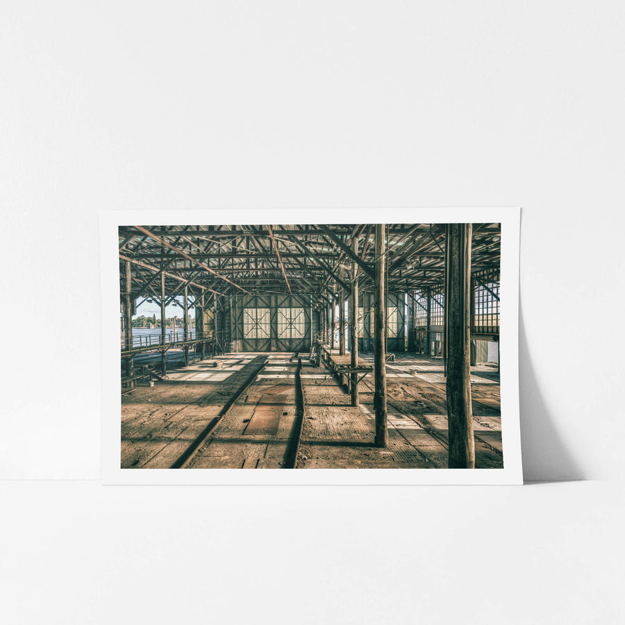 On the Catwalk at Halvorsens Boat Yard, steel columns rise from a worn timber floor, supporting a lattice of iron trusses.