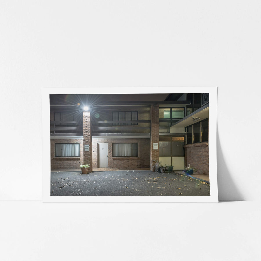 Oasis Resort at Hotel Motel 101, a single security light flares against the brick pillar between storeys, throwing hard.