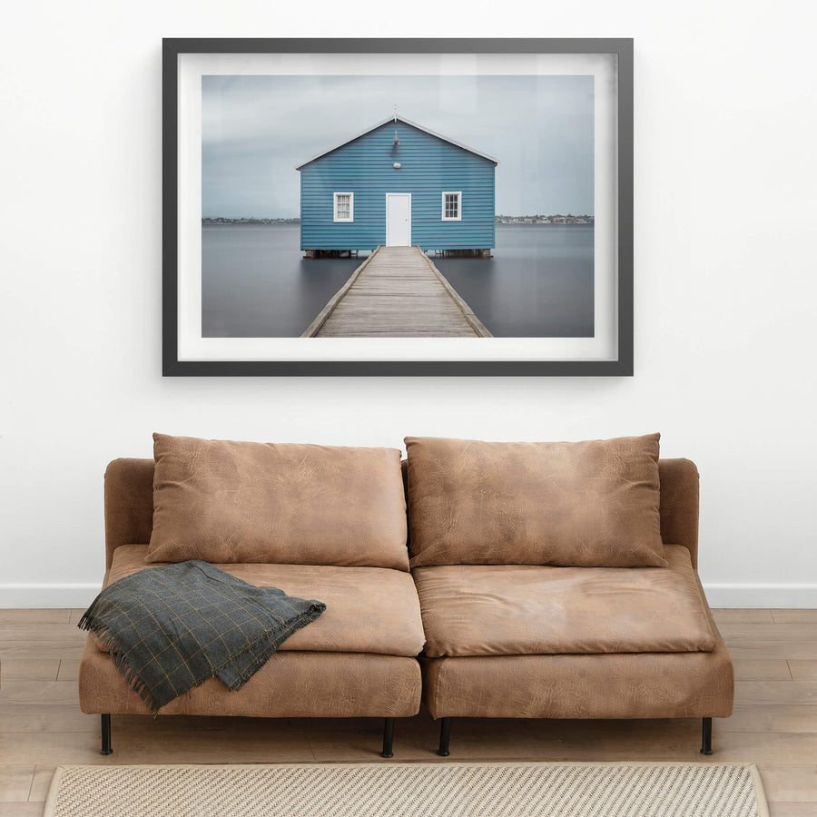 Crawley Edge Boatshed at Landscapes, a single blue timber boatshed sits on steel piles over flat grey water.