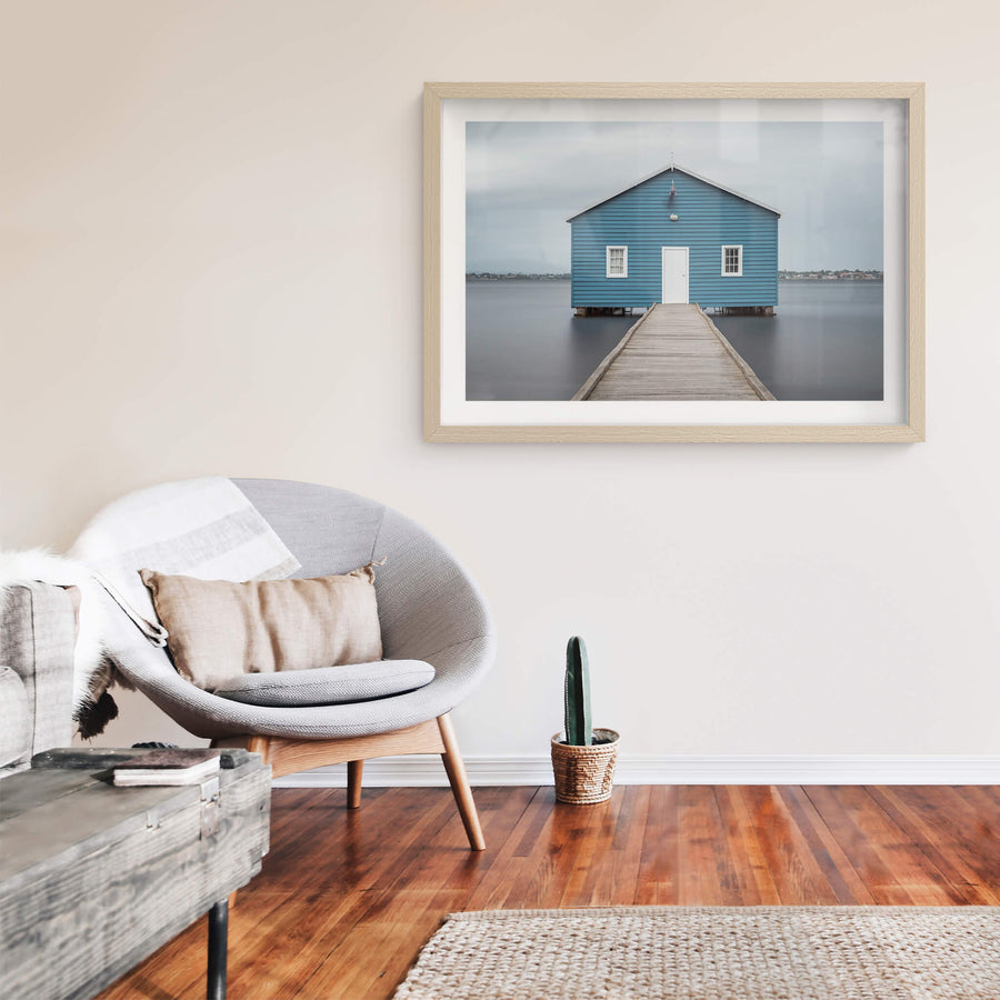 Crawley Edge Boatshed at Landscapes, a single blue timber boatshed sits on steel piles over flat grey water.