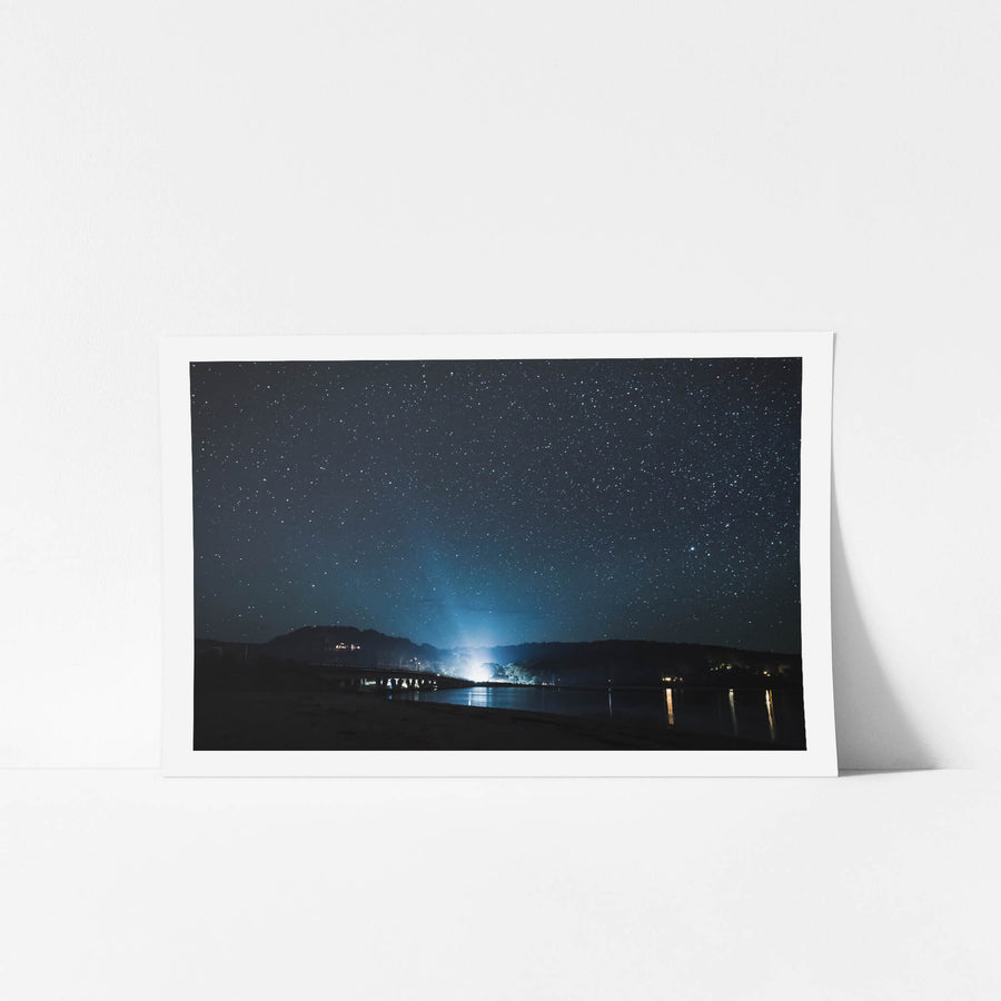 Tathra Bridge at Landscapes, headlights of a car approaching the Tathra Bridge under a dark and starry night sky.