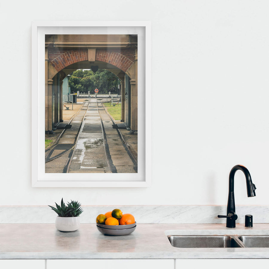 Entrance Rails at Newington Armory, narrow-gauge rail tracks run wet through a sandstone and brick archway, heading.