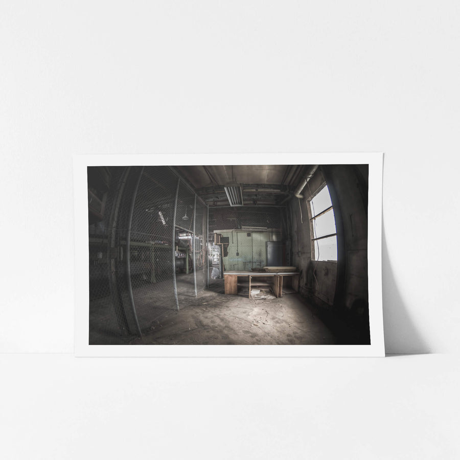 Caged Area at O-I Glass, a wooden desk sits near a large arched window, grey light falling across its surface.