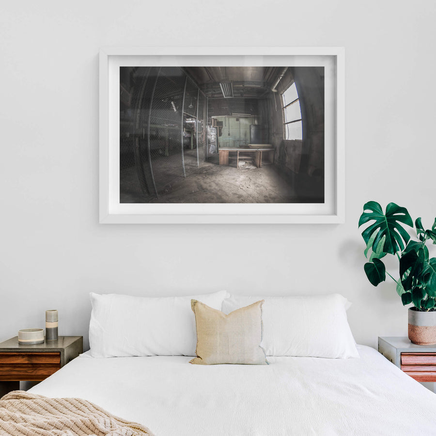 Caged Area at O-I Glass, a wooden desk sits near a large arched window, grey light falling across its surface.