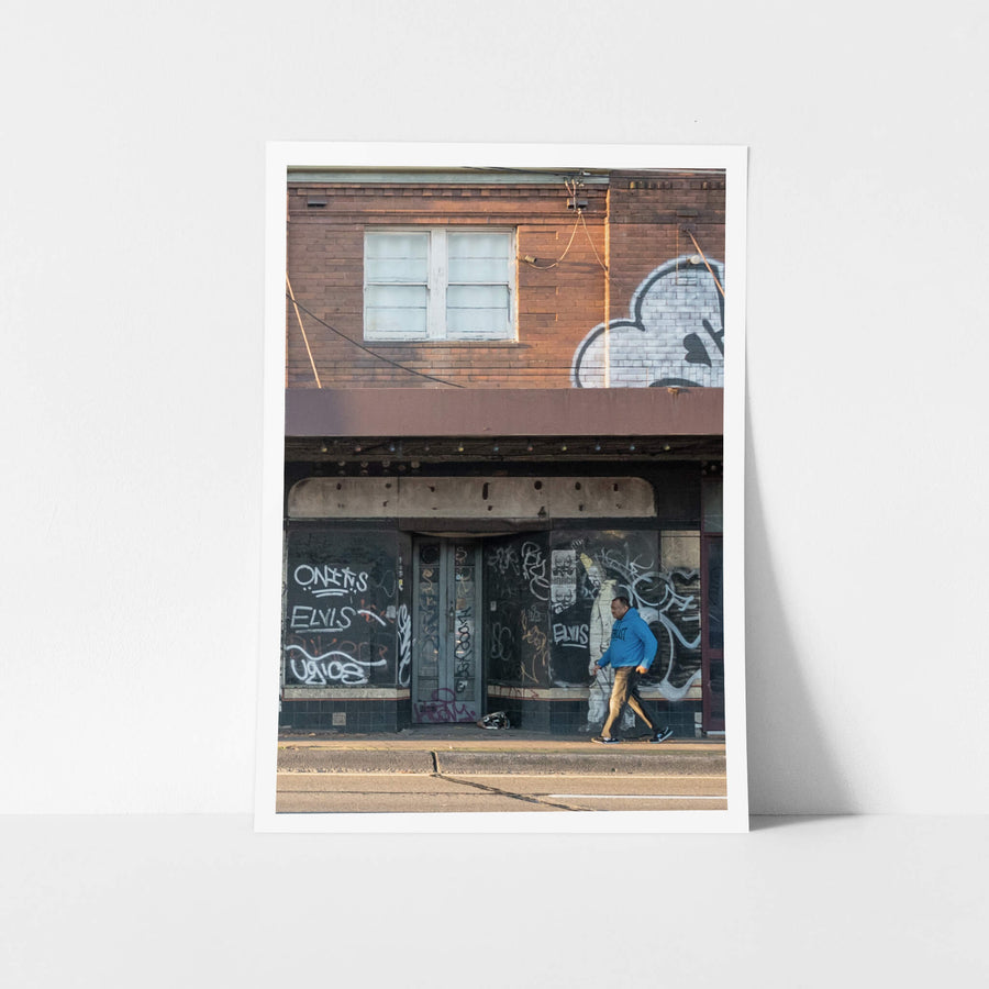 Passer By at Parramatta Road, a two-storey brick building sits hard against Parramatta Road.