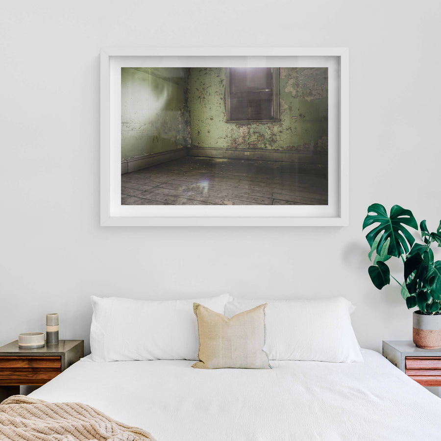 Bare Guest Room at Terminus Hotel, light seeps in through a boarded window, casting a dull glow across the floorboards.
