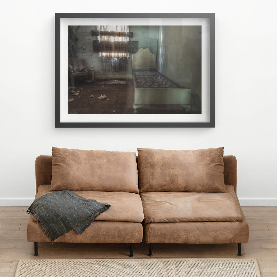 Guest Room at Terminus Hotel, a single bed frame sits along the wall, its bare springs exposed, beside a worn armchair.