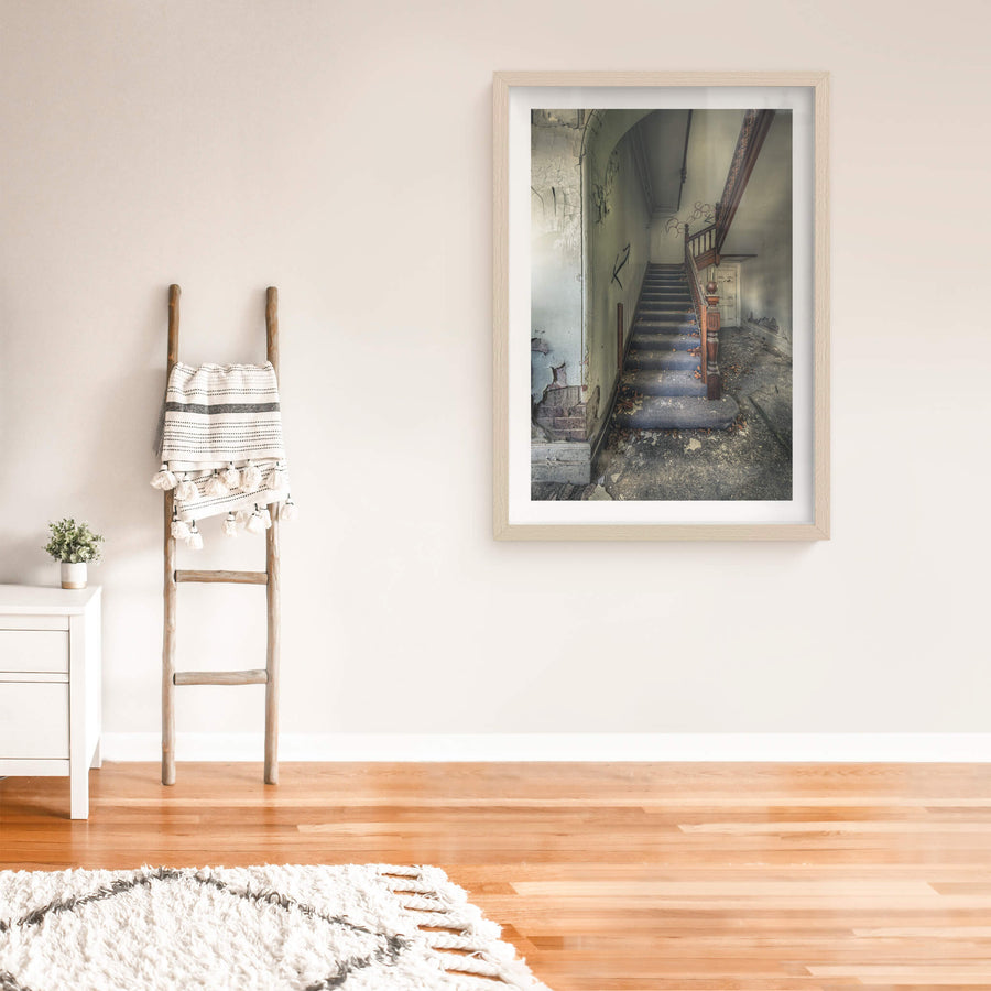 Crumbling Stairwell at The Asylum, a carved timber newel post stands at the base of a carpeted staircase.
