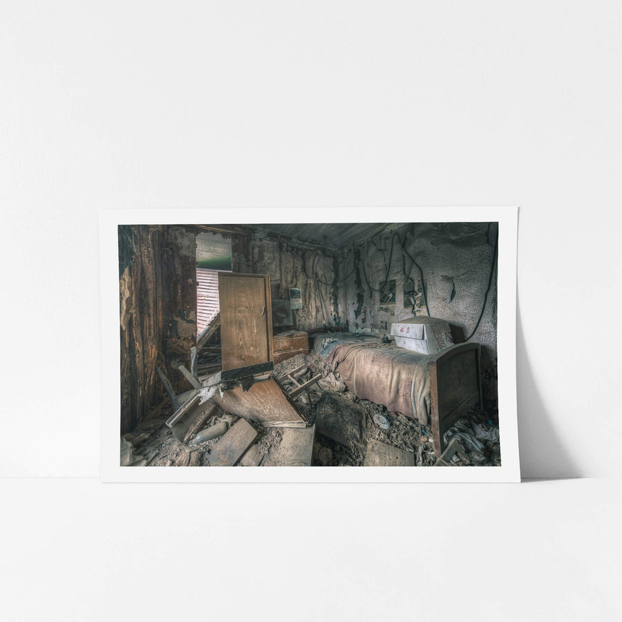 Life As It Was at The Post Office, a single bed sits against the back wall, a faded pink blanket still draped.