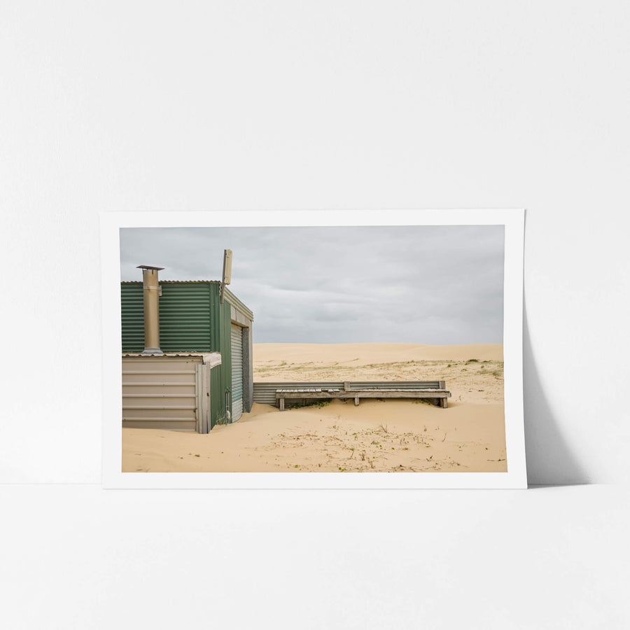 Boardwalk at Tin City, a corrugated iron shack sits half-buried in sand.