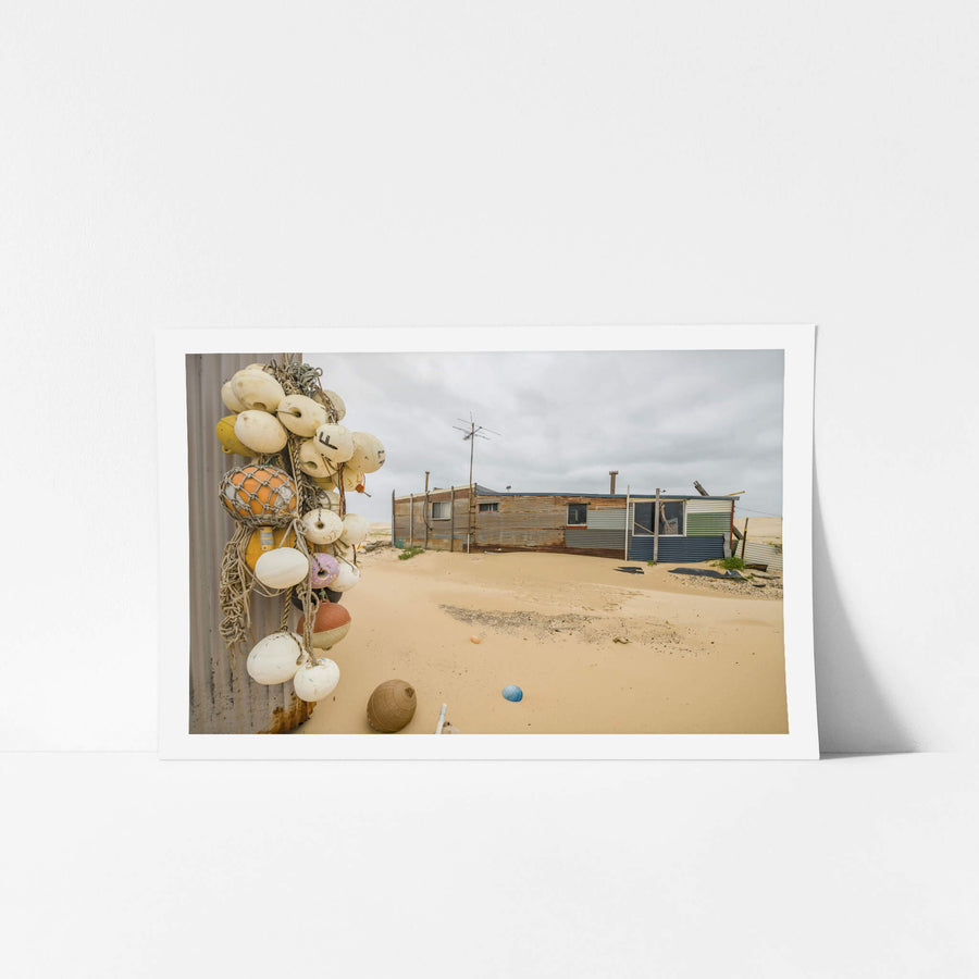 Buoys at Tin City, a cluster of fishing buoys hangs from a corrugated iron wall.