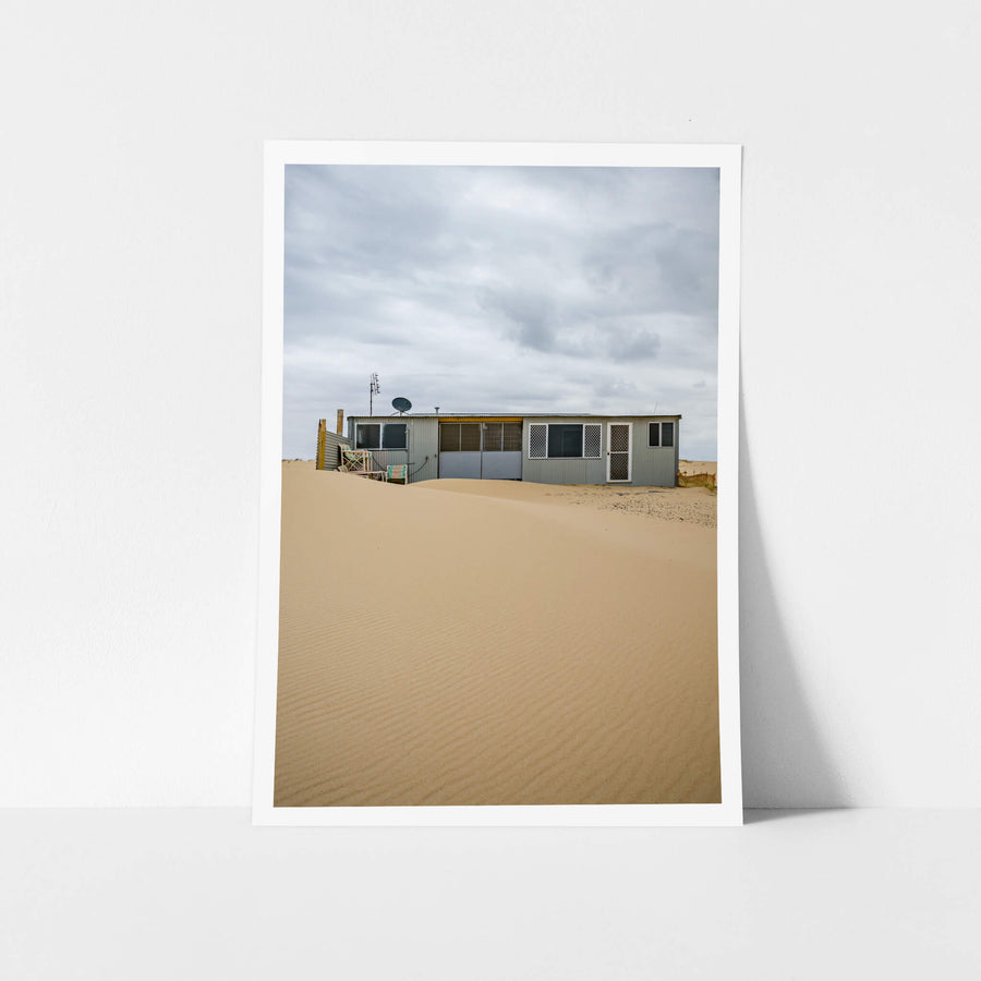 Ripples at Tin City, sand rises in a smooth, wind-rippled drift against a low corrugated iron shack.