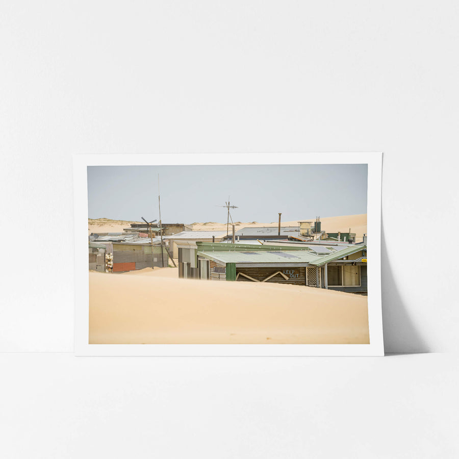 Rooftops at Tin City, sand rises to the rooflines of a cluster of makeshift shacks at Tin City.