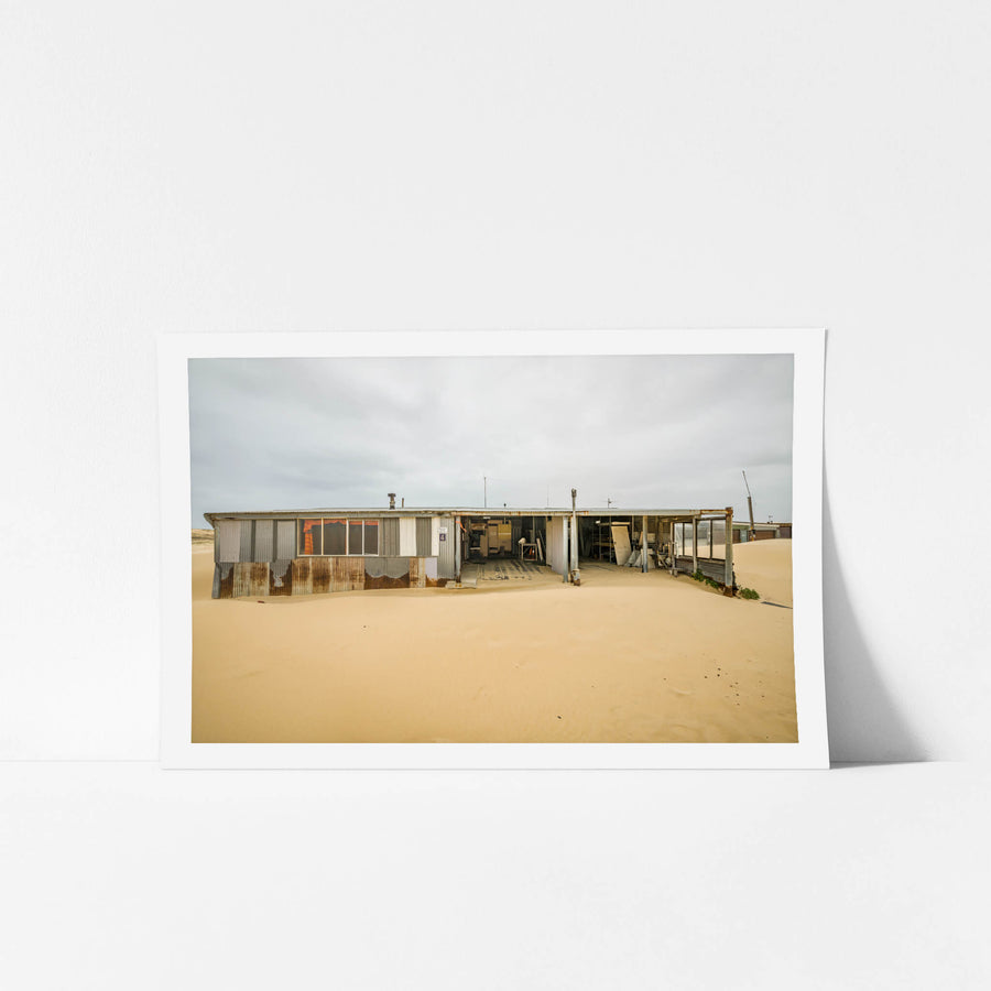 The Garage at Tin City, sand presses against the lower walls of a long, low shack at Tin City.
