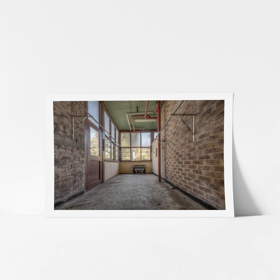 The Side Room at Waterfall Sanatorium, a narrow brick corridor leads toward a wall of steel-framed windows.