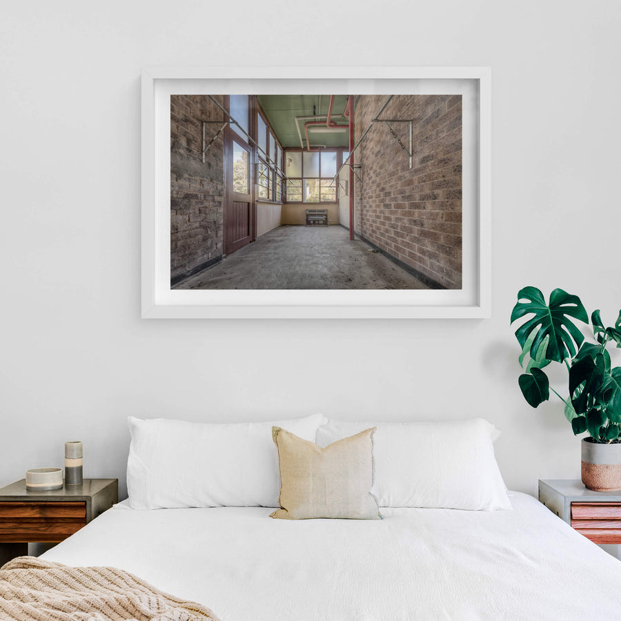 The Side Room at Waterfall Sanatorium, a narrow brick corridor leads toward a wall of steel-framed windows.